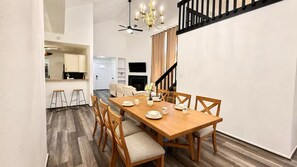 A dining area with a wooden table set for four, surrounded by chairs. A chandelier hangs from the ceiling, and a staircase with a black railing is visible to the right. - Spacious 4-bedroom house in wonderful Spring with AC (Spring)