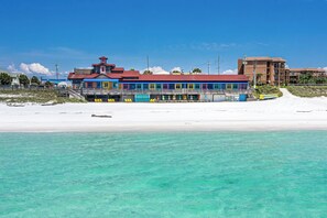 A beachfront hotel with a colorful building, a sandy beach, and clear turquoise water. - Stay Coastal. Stay Coconut / Closer to the beach. (Miramar Beach)