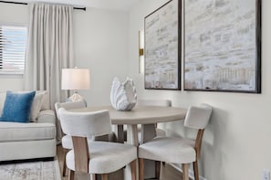 A dining area with a round table, four chairs, a decorative shell, and two abstract paintings on the wall. - Stay Coastal. Stay Coconut / Closer to the beach. (Miramar Beach)