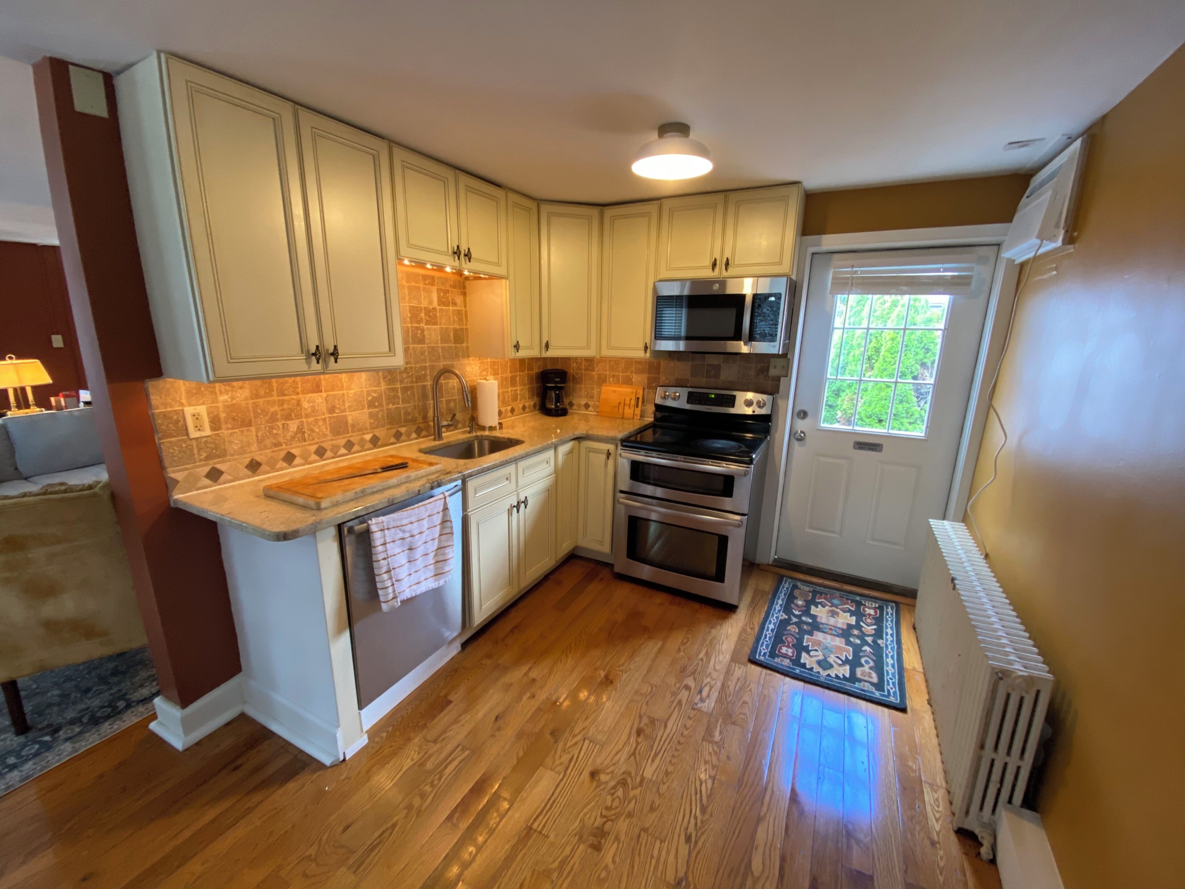 A kitchen with wooden flooring, white cabinets, a built-in microwave, and a stove.