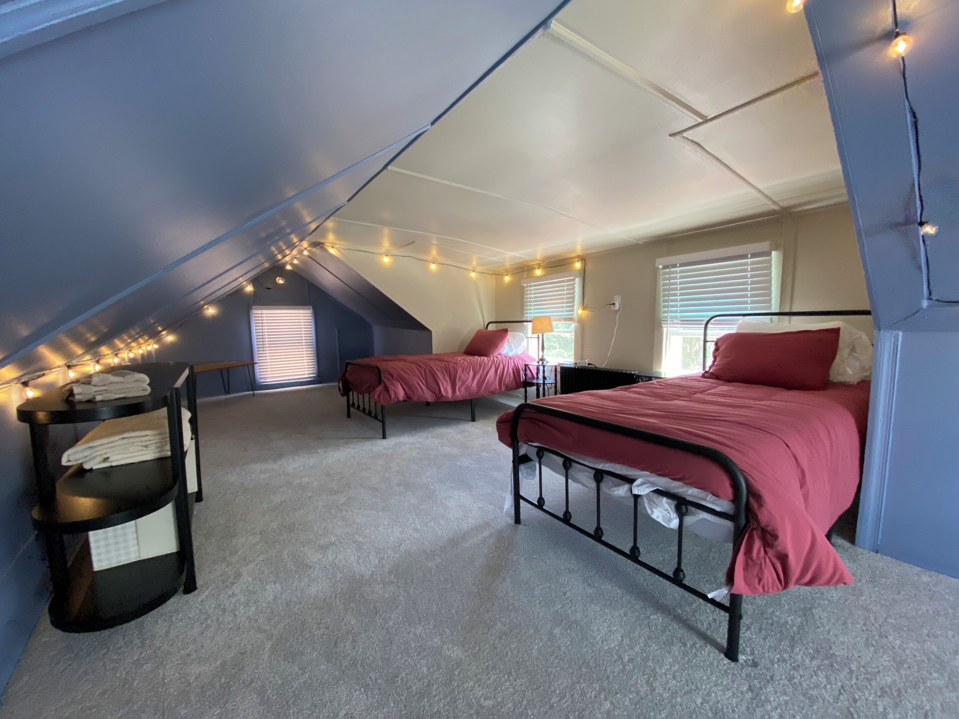 A bedroom with two beds, a radiator, a table with towels, and string lights.