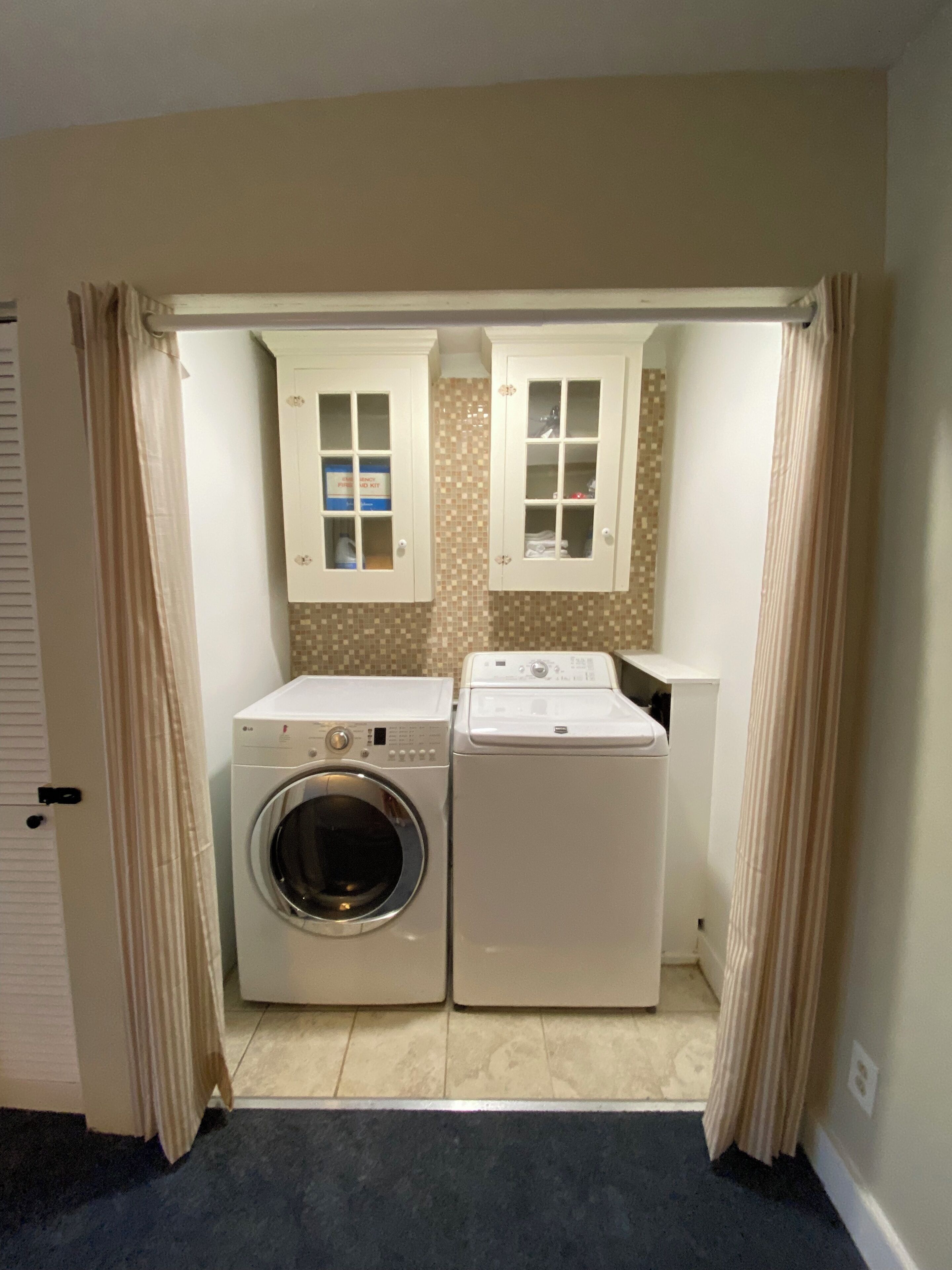 A laundry room with two washing machines, a dryer, and cabinets with storage space.