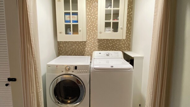 A laundry room with two washing machines, a dryer, and cabinets with storage space.