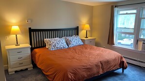 A bedroom with a bed, two bedside lamps, a window with a view, and a thermostat on the wall.