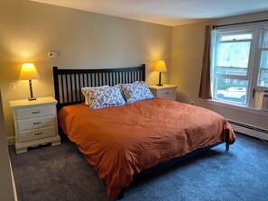 A bedroom with a bed, two bedside lamps, a window with a view, and a thermostat on the wall.
