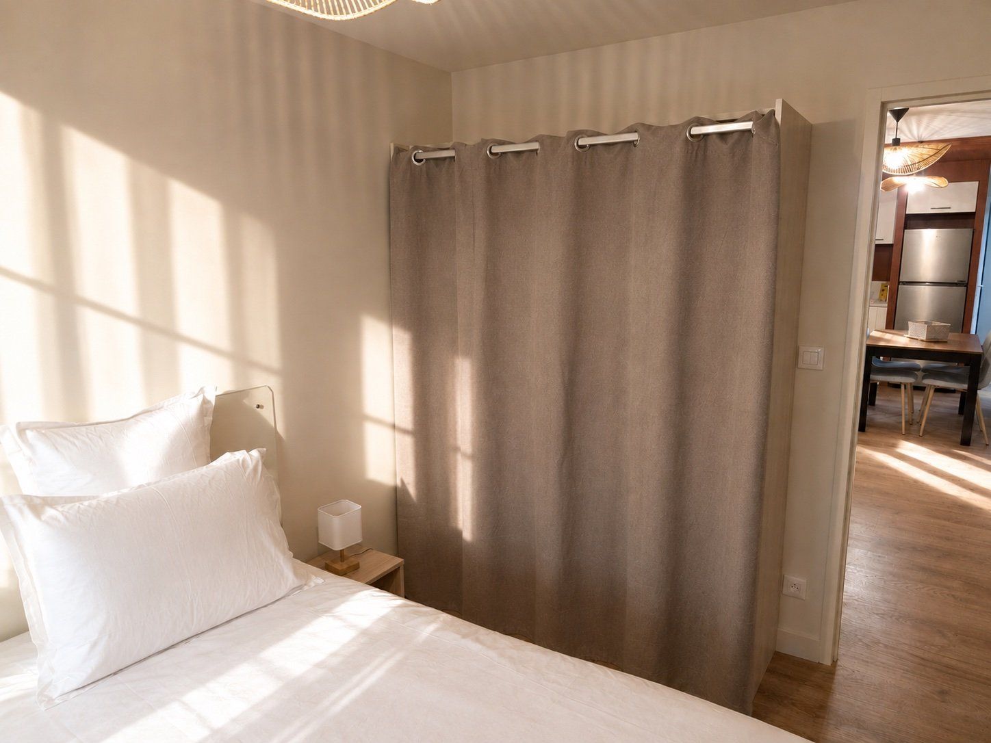 Ein Schlafzimmer mit einem Bett, einem Nachttisch, einer Lampe und Blick auf einen Küchenbereich.