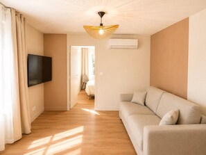 Ein modernes Wohnzimmer mit einem an der Wand befestigten Flachbildfernseher, einem beigen Sofa und einer Deckenleuchte.