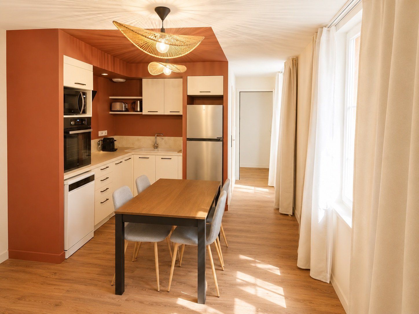 A modern kitchen with white cabinets, a stainless steel refrigerator, and a dining area with a wooden table and chairs.
