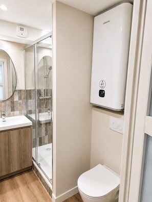 Ein Badezimmer mit einer Duschkabine, einer weißen Toilette und einem an der Wand montierten Warmwasserbereiter.