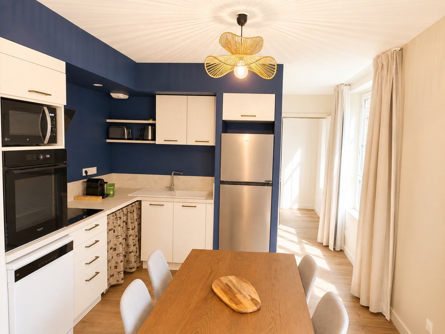 A compact kitchen with modern appliances, a dining area with a wooden table, and a ceiling light fixture.