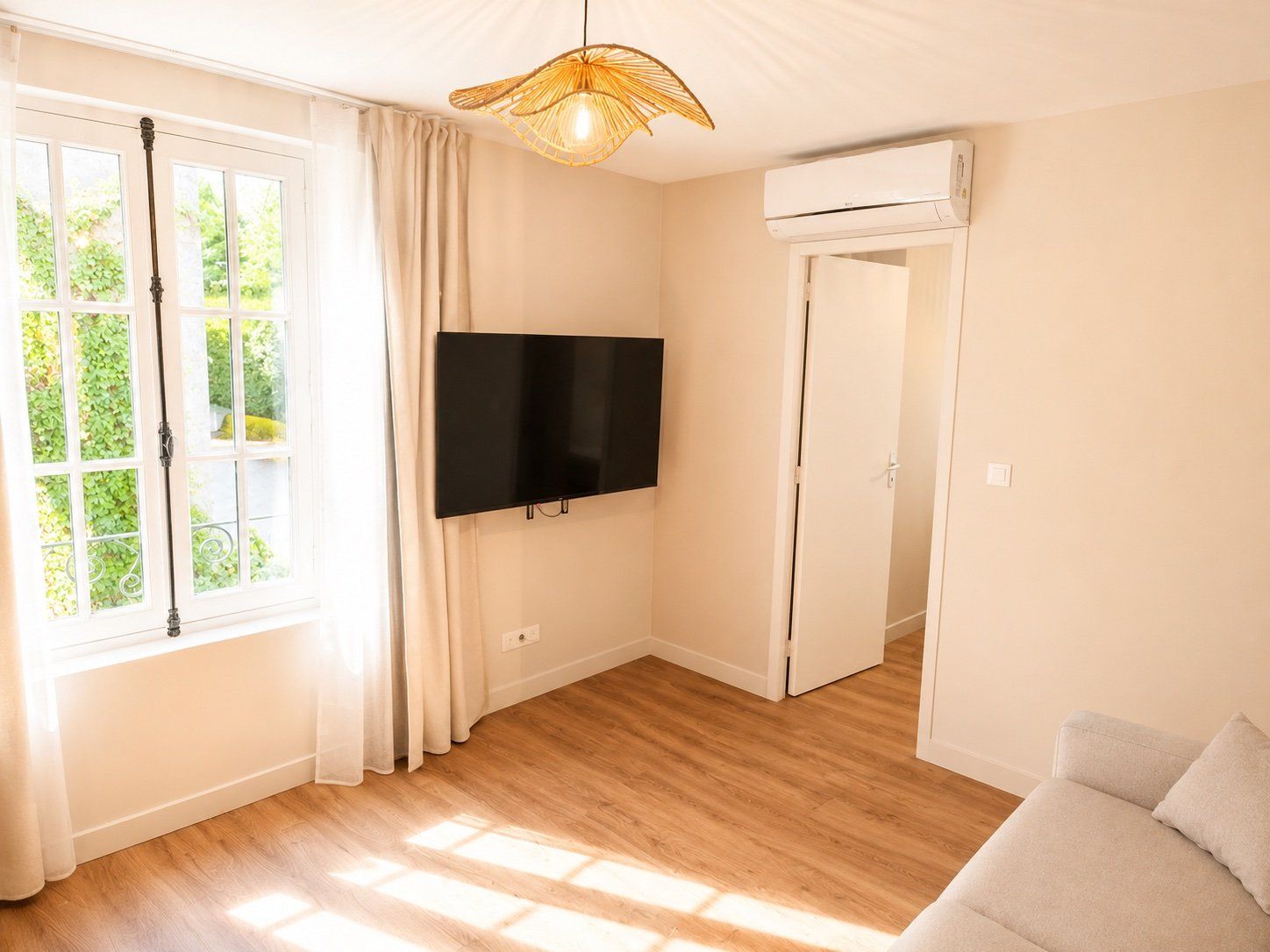 A room with a flat-screen TV mounted on the wall, a ceiling fan, and a door leading to another room.