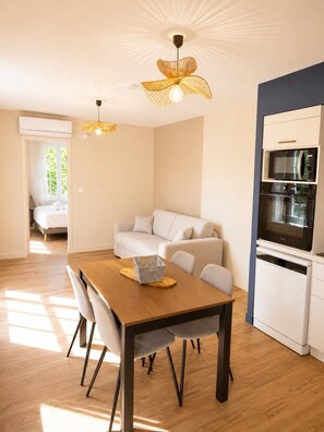 Een moderne keuken met een magnetron, oven en vaatwasser. Er is een eettafel met stoelen en een bank in de woonkamer.