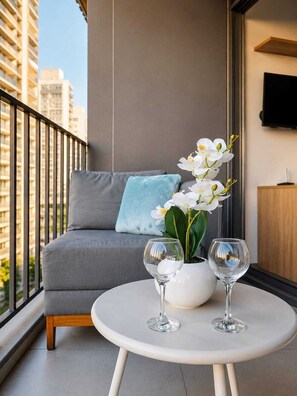 A balcony with a grey sofa, a small round table, two wine glasses, and a white orchid plant. - Premium Studio Augusta | Next Oscar Freire (São Paulo)