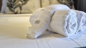 Ein ordentlich bezogenes Bett mit einem gefalteten weißen Handtuch und einem Kopfkissen mit Blättermuster.
