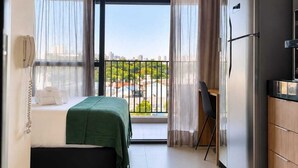 Ein Hotelzimmer mit Bett, Schreibtisch, Kühlschrank und einem Balkon mit Blick.