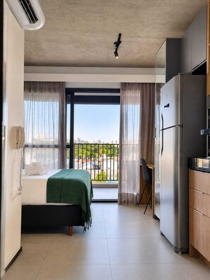 Habitació d'hotel amb un llit, una taula de treball, un refrigerador i un balcó amb vistes.