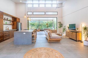 A spacious kitchen with a central island, wooden cabinets, and a large window offering a view of greenery. - Casa Tortuga Arriba in Ojochal (Osa)