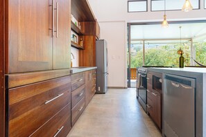 Een moderne keuken met houten kastjes, roestvrijstalen apparatuur en uitzicht op groen door een groot raam.