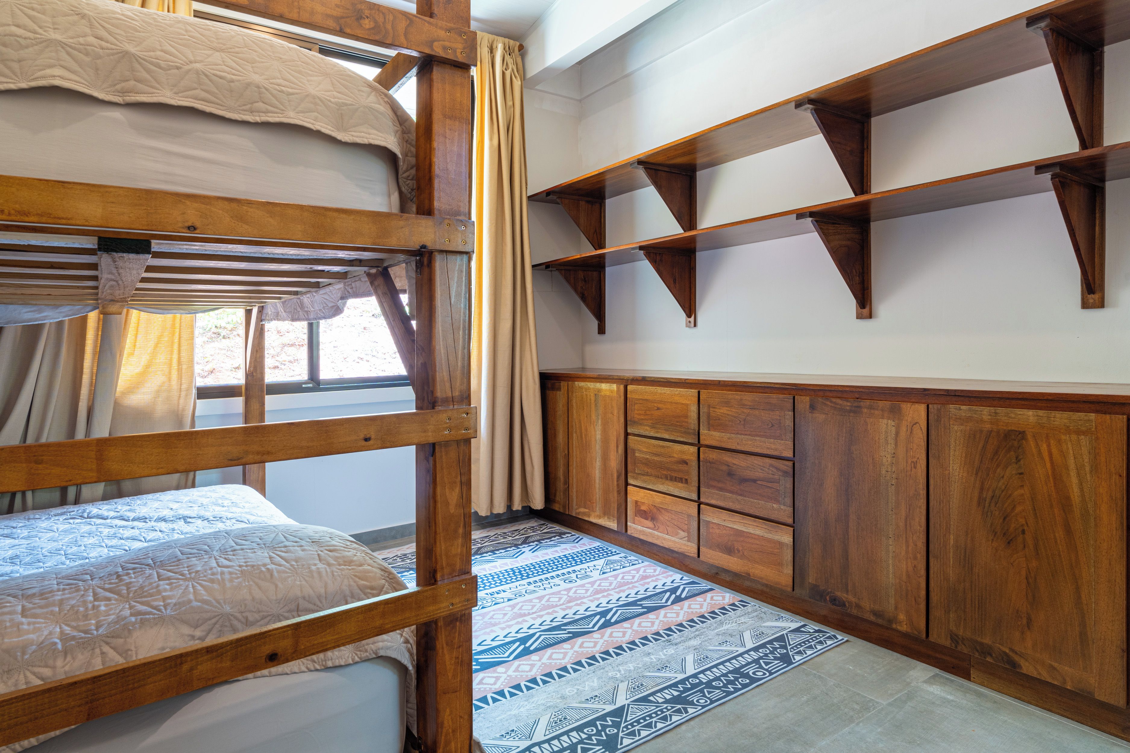 A bunk bed with a window, wooden shelves, and a patterned rug.