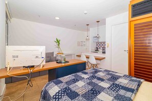 A compact hotel room with a bed, a desk, a chair, a small kitchen area, and a door. - Studio pr Ximo da Paulista Metr e Masp (São Paulo)