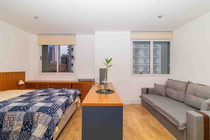A modern bedroom with a bed, a sofa, a small table, and a window with a view of buildings. - Studio pr Ximo da Paulista Metr e Masp (São Paulo)