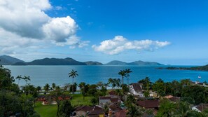 A coastal residential area with houses, palm trees, and a view of the sea and mountains. - Apto com Garagem a 600m da Praia das Toninhas (Ubatuba)