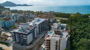 A coastal urban area with multi-story buildings, a swimming pool, and a view of the sea. - Apto com Garagem a 600m da Praia das Toninhas (Ubatuba)