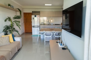 A modern kitchen with white cabinets, a built-in oven, and a dining area with white chairs. - Apto com Garagem a 600m da Praia das Toninhas (Ubatuba)