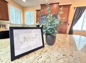 A kitchen with a welcome sign, a potted plant, granite countertops, wooden cabinets, and a window with blinds. - Feel at Home in Stone Oak @great for Weeks/Months /3 beds 2.5 baths- Gated (San Antonio)