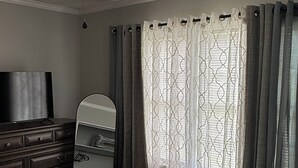 A bedroom with a bed, a dresser, a television, a ceiling fan, and a window with curtains. - The Cove #2. Lovely 2-bedroom apartment with AC in charming Rockingham. (Rockingham)