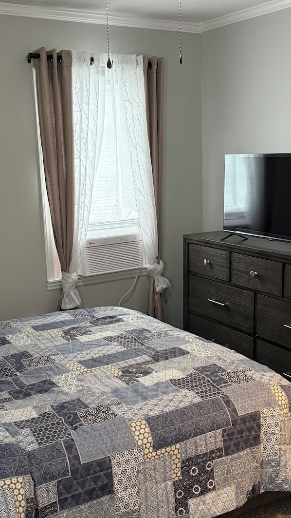 A bedroom with a bed, a dresser, a television, and a window with curtains.