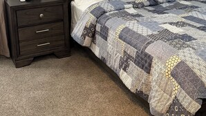 A bedroom with a bed, nightstand, lamp, and a carpeted floor.