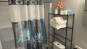 A bathroom with a shower curtain, toilet, sink, and a shelf with towels. - The Cove #2. Lovely 2-bedroom apartment with AC in charming Rockingham. (Rockingham)