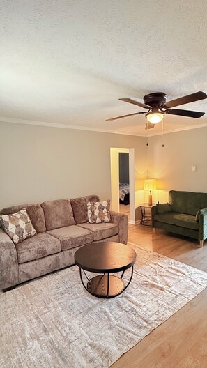A living room with a sofa, a round coffee table, a ceiling fan, and a lamp. - The Cove #2. Lovely 2-bedroom apartment with AC in charming Rockingham. (Rockingham)
