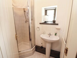 Ein Badezimmer mit einer Duschkabine, einem weißen Waschbecken und einem Fenster über dem Spiegel.