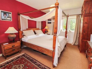 Ein Bett mit Baldachin, ein Nachttisch mit Lampe, eine hölzerne Kommode und ein gemustertes Teppich.