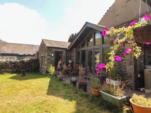 Ein Haus aus Stein mit geneigtem Dach, einer Steinmauer und einem Garten mit Blumentöpfen und Blumen.