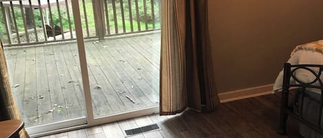 A room with a wooden floor, a sliding glass door leading to an outdoor deck, a chair, and a bed.