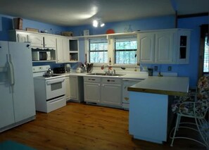 A kitchen with white cabinets, a microwave, a sink, and a wooden floor. - Big Cottage, sleeps 21 close to Lake Ouachita! (Mount Ida)