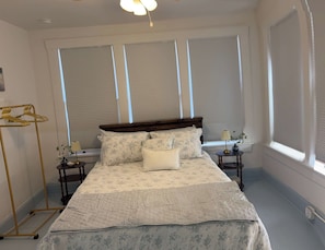 A bedroom with a bed, two bedside tables, a hanging light fixture, and a window with blinds. - Renovated Apartment Downtown HS (Hot Springs)