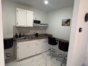 A compact kitchen with white cabinets, a microwave, a sink, and two bar stools. - Renovated Apartment Downtown HS (Hot Springs)