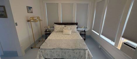 Un dormitorio con cama, ventilador de techo, ventana con persianas y radiador.