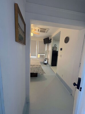 A narrow hallway leading to a bedroom with a bed, a television, and a clock on the wall. - Renovated Apartment Downtown HS (Hot Springs)