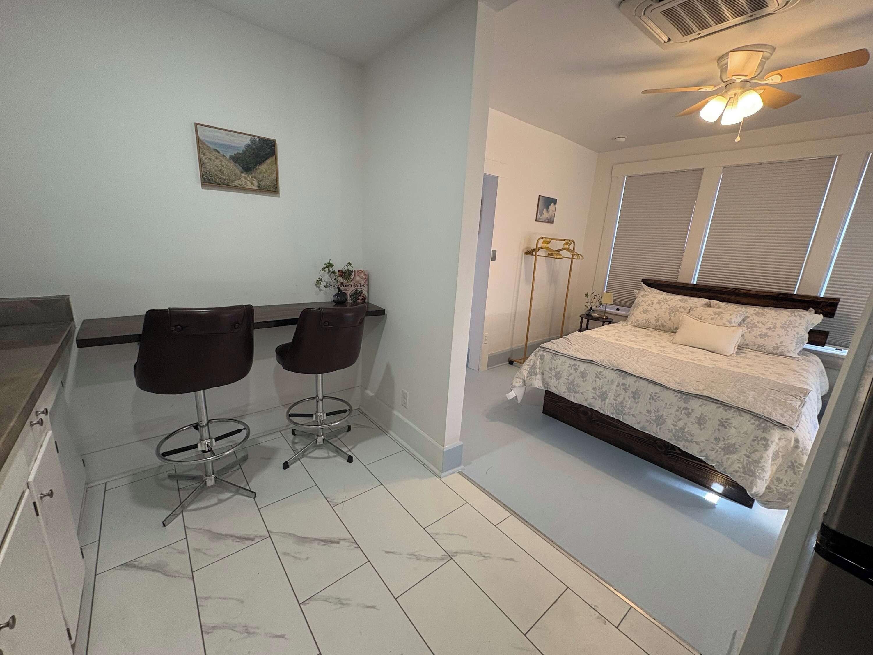 Ein Schlafzimmer mit Bett, Nachttisch, Lampe, Deckenventilator und Fenster mit Jalousien.