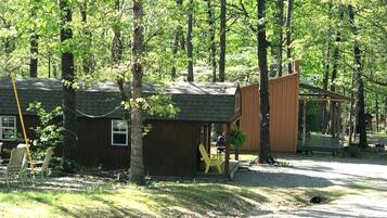 A cabin with a porch, a small deck, and a covered outdoor seating area surrounded by trees.