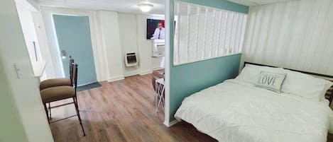 Una habitación con cama, una silla, un televisor y una ventana con persianas.