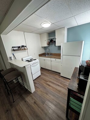 A compact kitchen with white cabinets, a stove, a sink, and a refrigerator. - The Hideout downtown Hot Springs (Hot Springs)