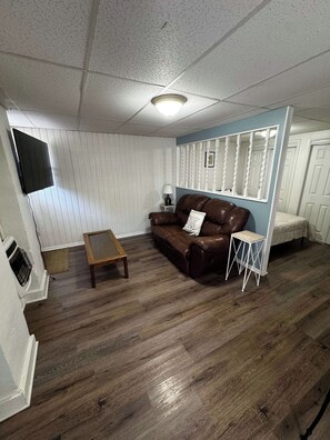 A room with a brown leather sofa, a wooden coffee table, a small white side table, a television mounted on the wall, and a door with a white frame. - The Hideout downtown Hot Springs (Hot Springs)