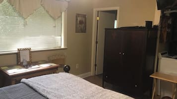 A bedroom with a bed, a desk with a chair, a wardrobe, and a television.