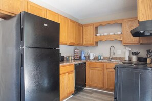 Une cuisine avec des meubles de rangement en bois, un réfrigérateur noir, une cuisinière et divers appareils électroménagers.